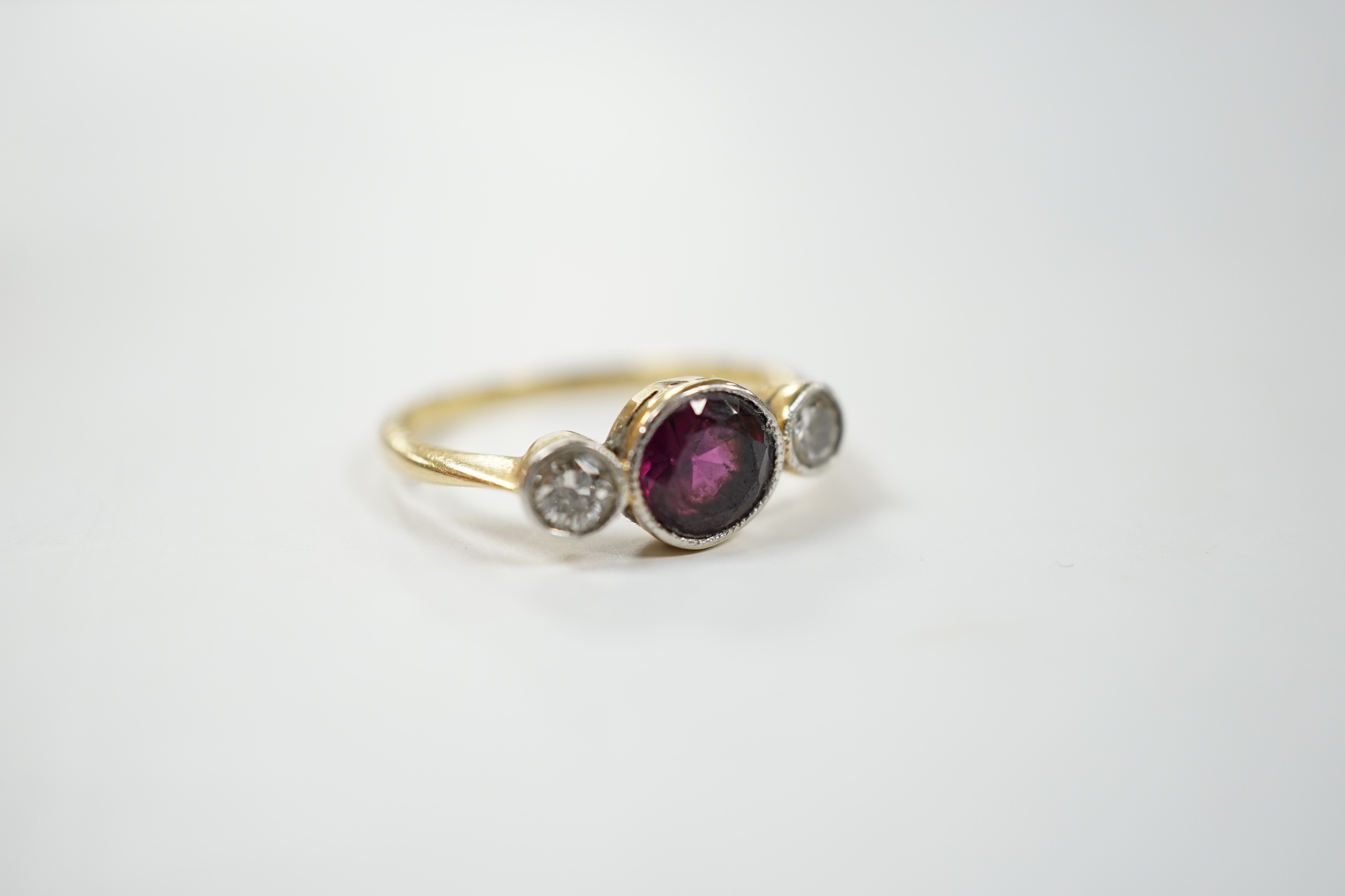 An early 20th century yellow metal and millegrain set single stone garnet and two stone diamond ring, size M, gross weight 2.8 grams.